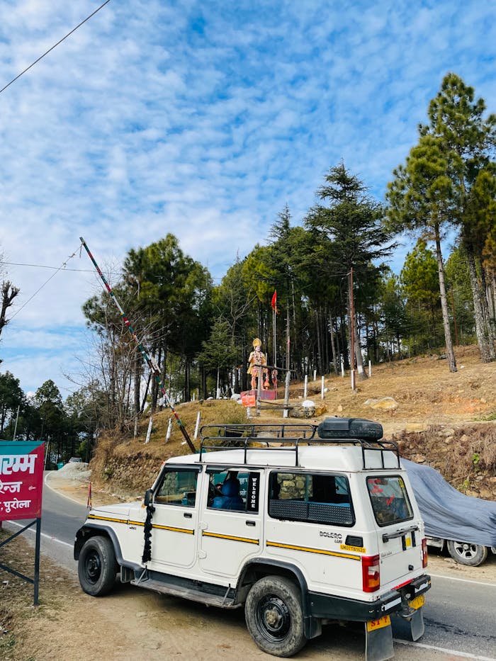 A white jeep traveling on a scenic mountain road beside a statue under a blue sky.