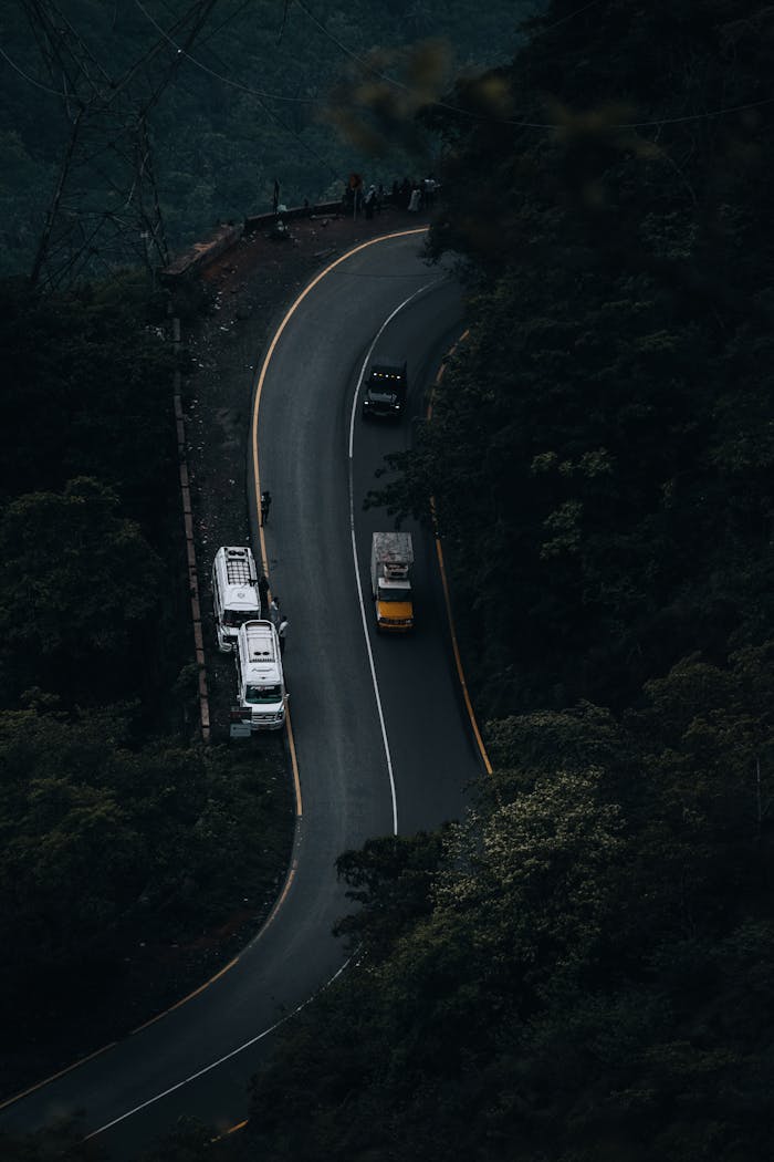 digital-01 An aerial shot of a curved mountain road with trucks navigating through dense forest on a misty day.