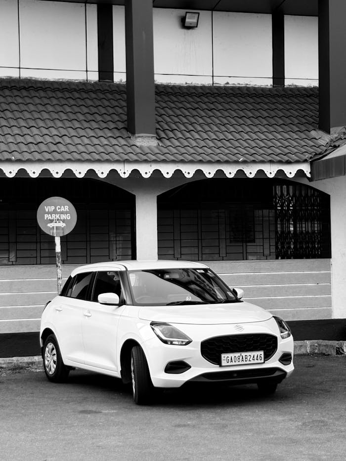 Black and white photo of a white car parked in a VIP spot in GA, India.